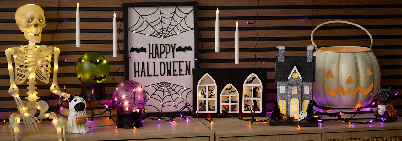 Halloewen string lights and light-up hanging candles, light-up skeleton and wall art, haunted house, jack-o-lanterns, & more on an entryway table.