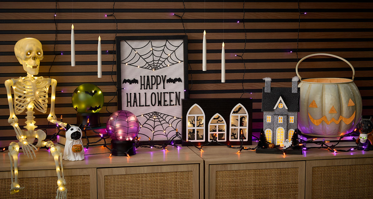 Halloewen string lights and light-up hanging candles, light-up skeleton and wall art, haunted house, jack-o-lanterns, & more on an entryway table.