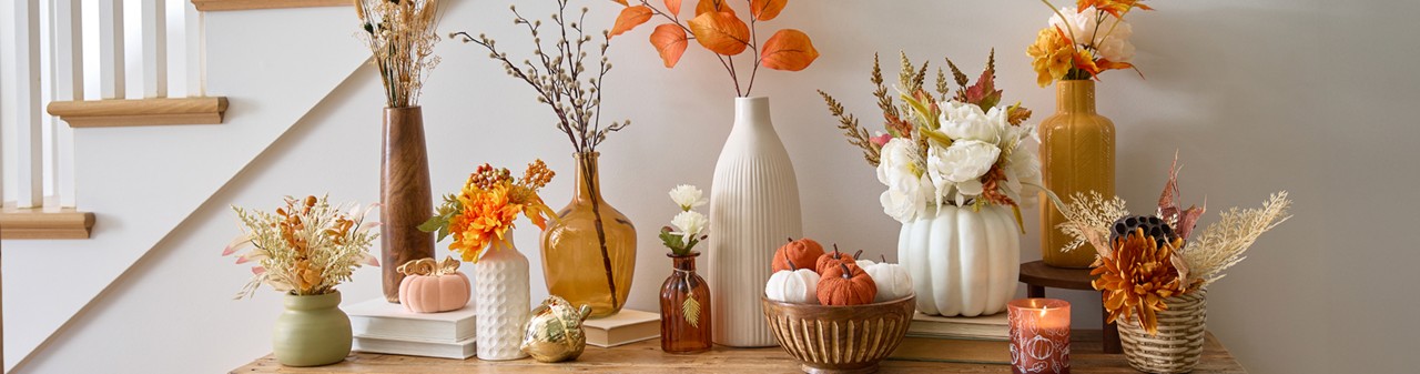 Fall floral bushes, branches, and picks in vases and premade fall floral arrangements on an entryway table.