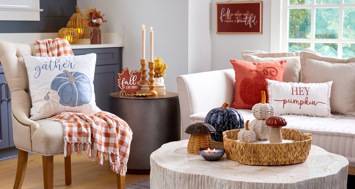 Den decorated for fall with pumpkin pillow, throw, pumpkin decor, fall candles, and fall floral.