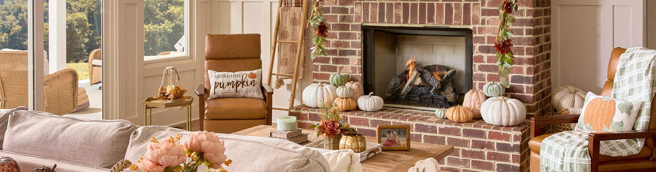 Den decorated for fall with pumpkin pillows, fall pillows and throws, pumpkin and fall decor, fall candles, and fall floral.