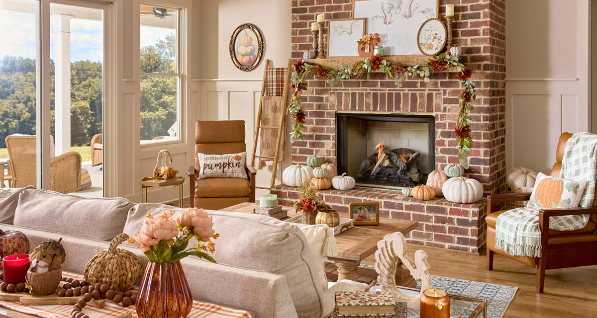 Den decorated for fall with pumpkin pillows, fall pillows and throws, pumpkin and fall decor, fall candles, and fall floral.
