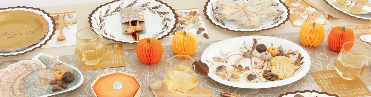 Fall party table set with pumpkin, turkey, and leaf shaped plates, round harvest plates, napkins, gold party utensils, and fall & pumpkin table decor.