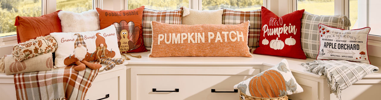 Fall pillows and throws in various colors and designs on a bay window bench.