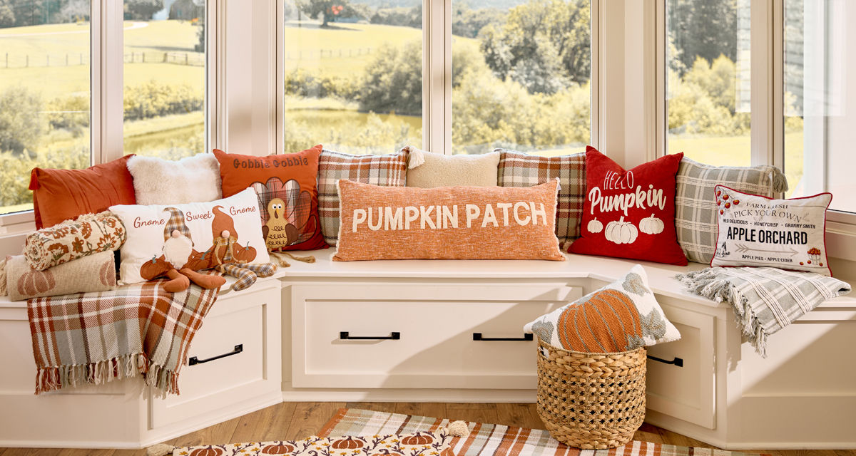 Fall pillows and throws in various colors and designs on a bay window bench.