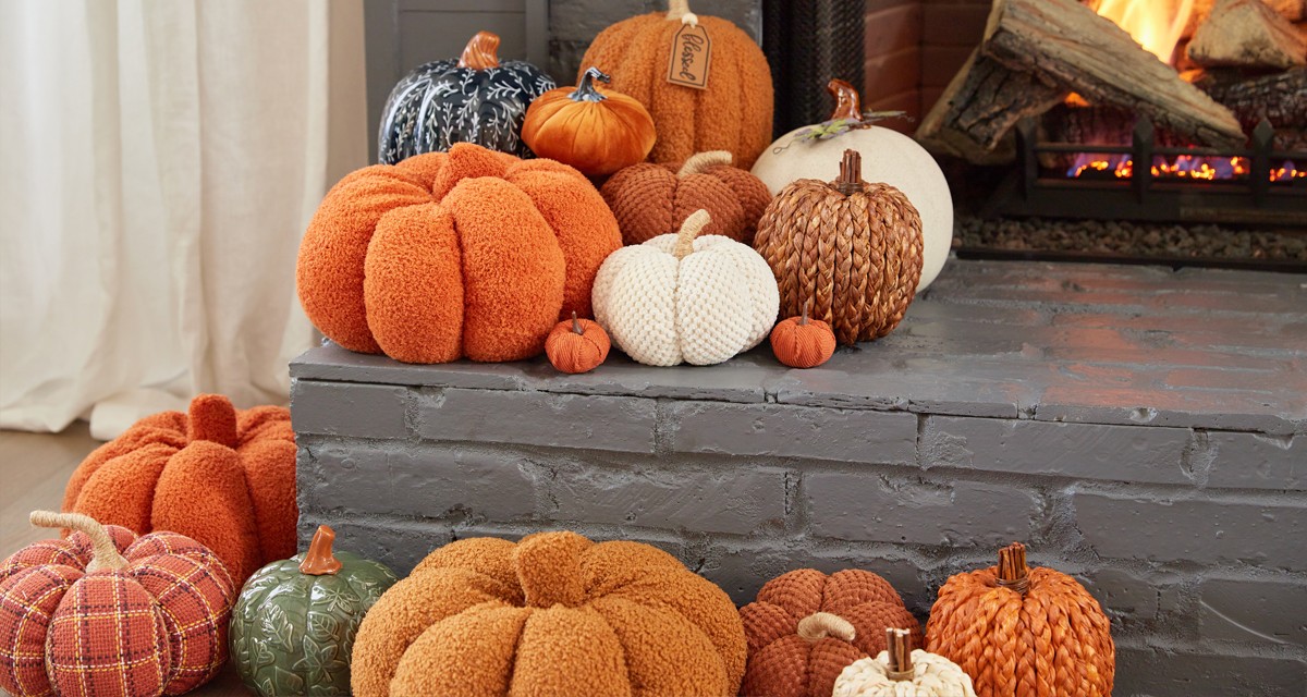 Pumpkins from pOpshelf in various sizes, textures, and colors pilled on either side of a lit fireplace.