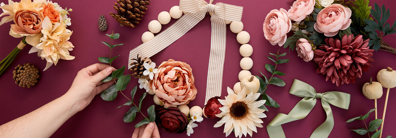 Woman decorating a bead wreath with fall florals & picks, fall ribbon, and pumpkin embellishments.