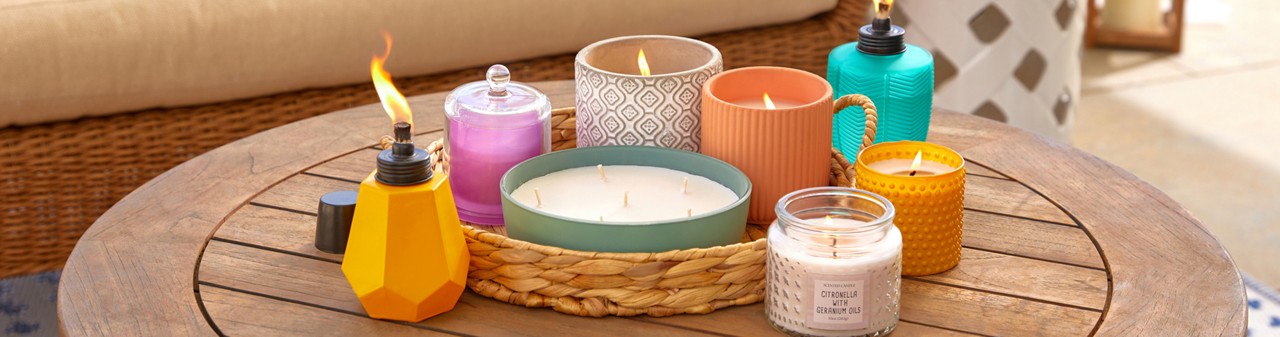 Citronella candles and torches from pOpshelf in various sizes, designs, and colors on a wooden porch table.