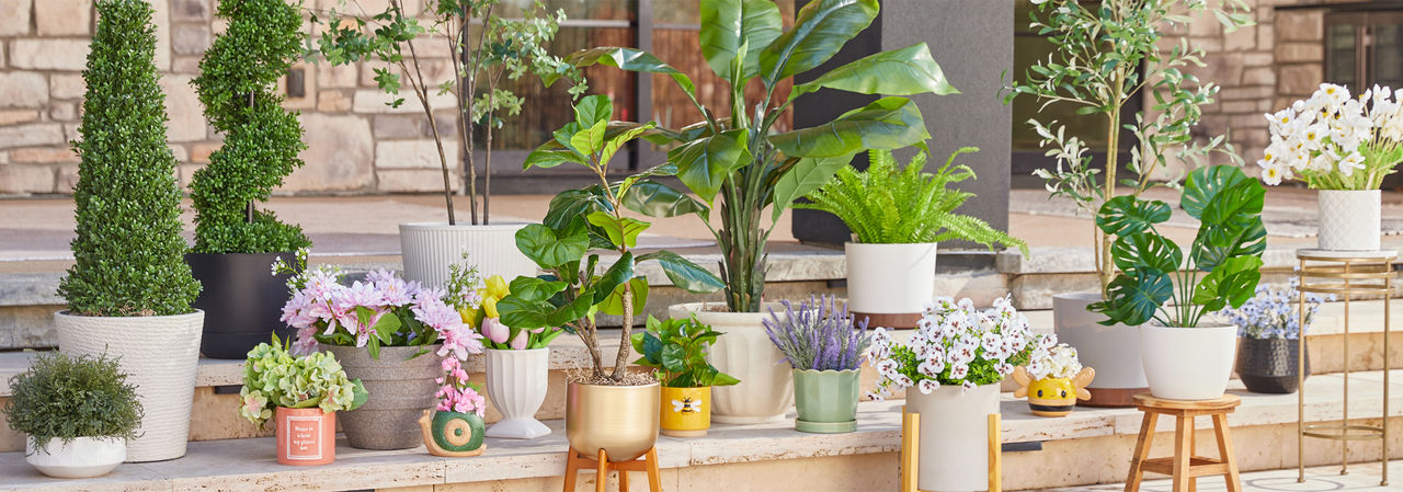 Various colors and designs of pOpshelf outdoor planters, flower pots, and plant stands filled with greenery and flowers on a patio.