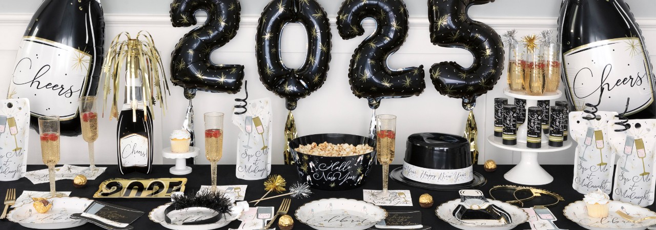 Party table set for New Year's Eve with champagne bottle balloons, foil fringe and Happ New Year  banners, 2025 ballons, party plates, cups, napkins, and favors from pOpshelf. 