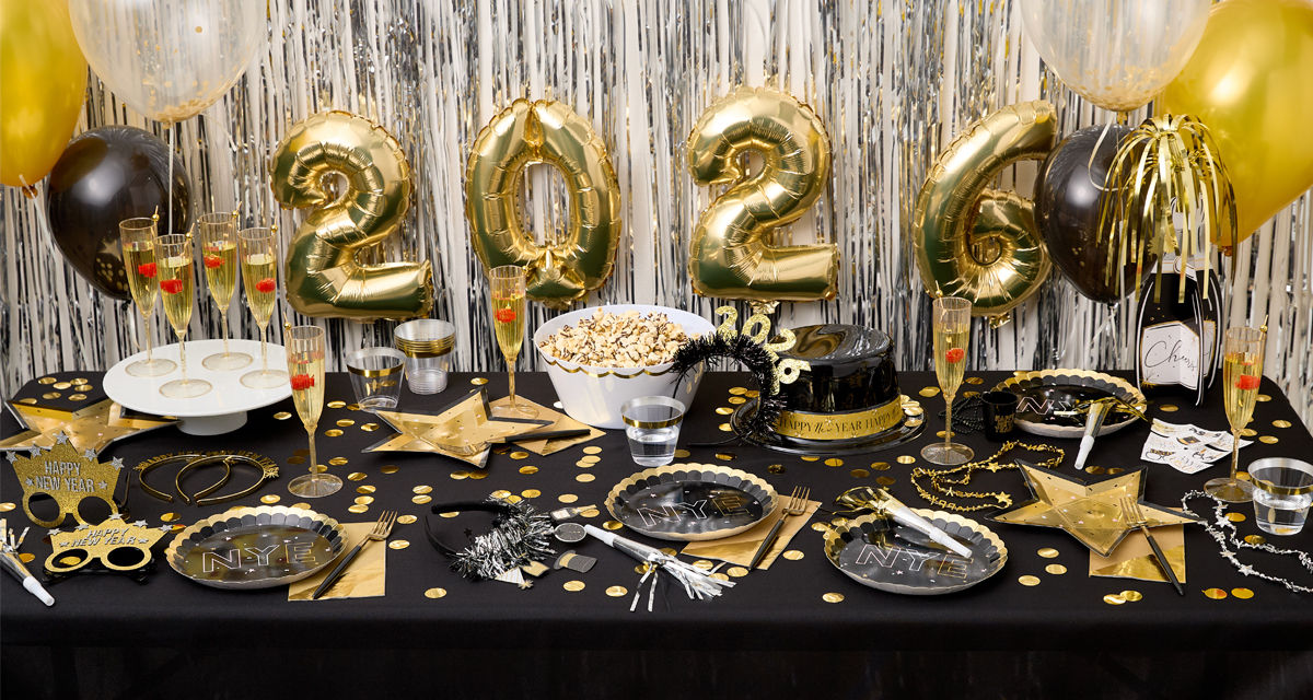 Party table set for New Year's Eve with champagne bottle balloons, foil fringe and Happ New Year  banners, party plates, cups, napkins, and favors from pOpshelf. 