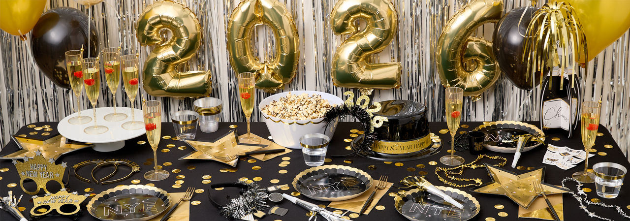 Party table set for New Year's Eve with champagne bottle balloons, foil fringe and Happ New Year  banners, party plates, cups, napkins, and favors from pOpshelf. 