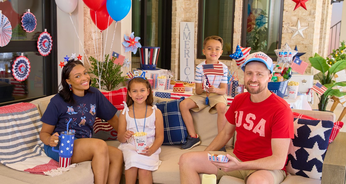Family enjoying a backyard BBQ with patriotic decor, party supplies, and apparel.