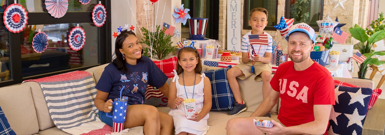 Family enjoying a backyard BBQ with patriotic decor, party supplies, and apparel.