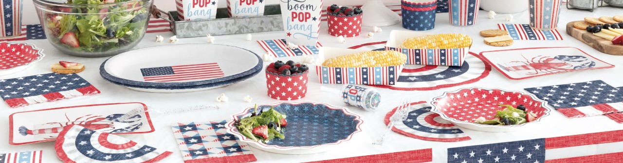 Table set with red, white & blue patriotic party supplies from pOpshelf: lobster and flag paper plates, flag and stars & stripes paper napkins, popcorn and hotdog holders, tablecovers, party decorations & more.
