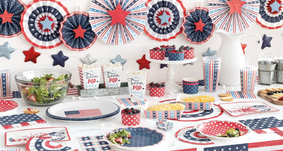 Table set with red, white & blue patriotic party supplies from pOpshelf: lobster and flag paper plates, flag and stars & stripes paper napkins, popcorn and hotdog holders, tablecovers, party decorations & more.