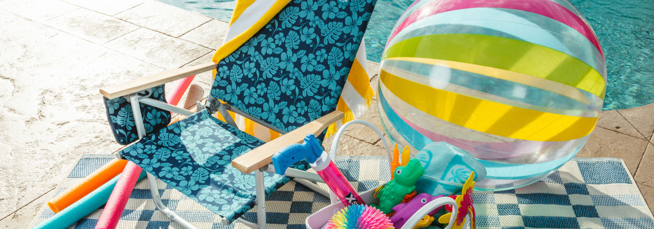 Blue folding beach chair by pool with beach towels, beach bag, pool toys & more