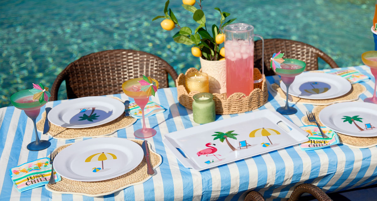 Poolside table set with colorful melamine dinnerware with summer icons, ice bucket, and plastic margarita glasses.