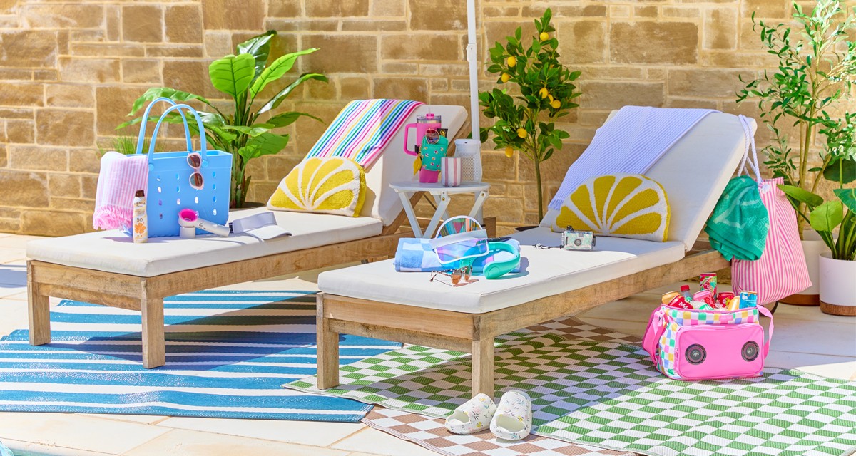 Lounge chairs with towels, pillows, white side table, rainbow umbrella, cooler, tote bags & accessories.