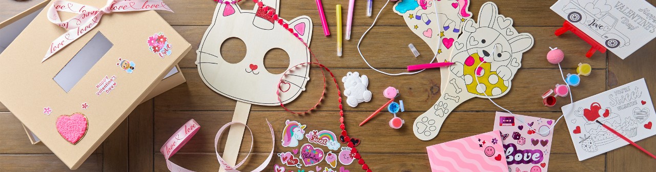 Table covered with various Valentine's day crafts: DIY valentine's wooden masks and paddle ball sets, kits, valentines ribbon, plaster and canvas craft kits, and more.