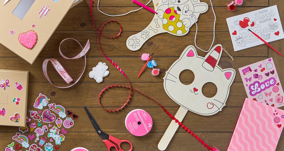 Table covered with various Valentine's day crafts: DIY valentine's wooden masks and paddle ball sets, kits, valentines ribbon, plaster and canvas craft kits, and more.