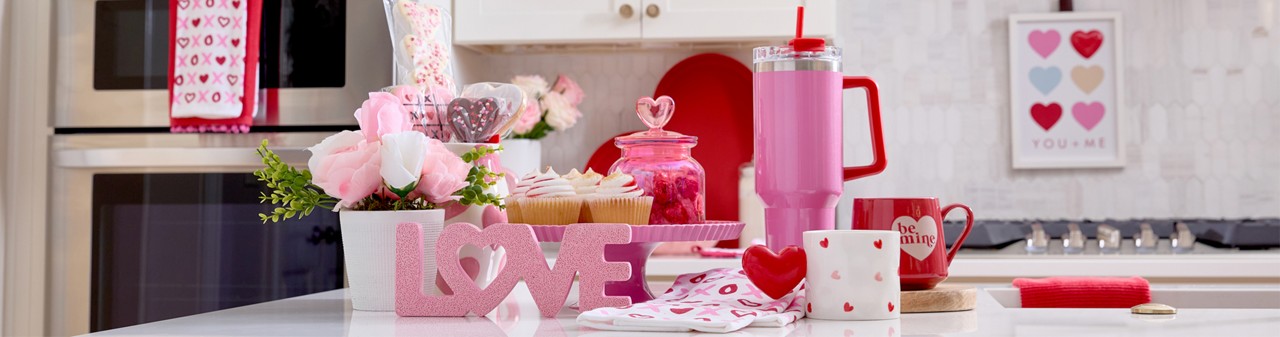 Kitchen island with Valentine's cake stand, mugs, travel cup, flowers, candy  & Valentine's Day kitchen linens.