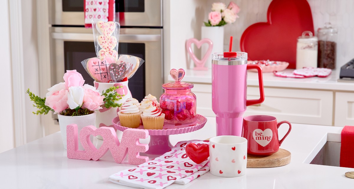 Kitchen island with Valentine's cake stand, mugs, travel cup, flowers, candy  & Valentine's Day kitchen linens.