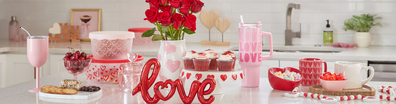 Kitchen island with Valentine's cake stand, mugs, travel cup, flowers, candy  & Valentine's Day kitchen linens.
