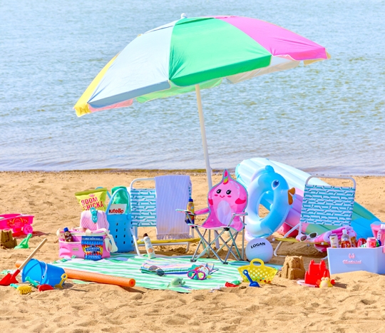 Beach scene with folding beach chairs, beach umbrella, beach towels, insulated coolers & sand toys.