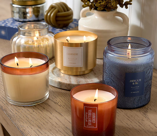 A wooden entryway table is decorated with orange, terracotta, cream, brass, and dark blue western-inspired candles.