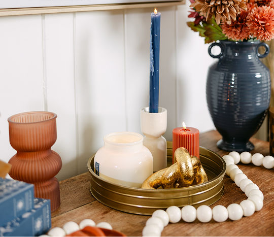 A wooden entryway table is decorated with orange, terracotta, cream, brass, and dark blue western-inspired decor including candles, vases, and decorative accents.