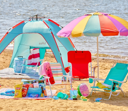 Beach scene with folding beach chairs, beach umbrella, beach tent, beach towels, insulated coolers & sand toys.