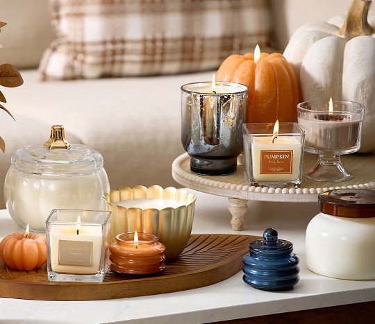 A coffee table is set with seasonal fall candles from pOpshelf in pumpkin shapes, glass jars, tin jars, and an autumn floral vase filled with fall leaf stems.