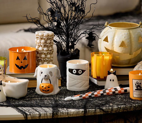 A table features a close-up shot of various Halloween themed candles from pOpshelf including a skeleton in a bath tub, a small ghost wearing a bow, a dog sheet ghost holding a trick-or-treat pumpkin, and other fun Halloween aesthetic candles.