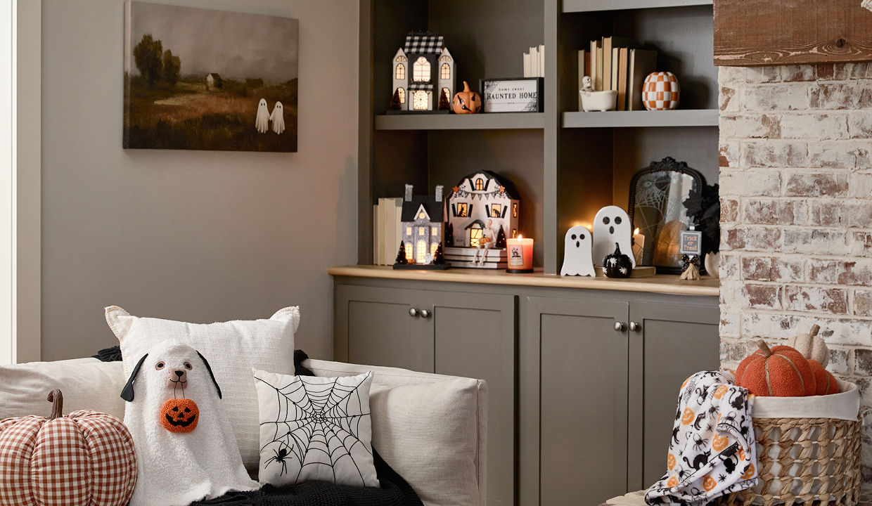 A neutral toned living room is decorated with classic Halloween decor from pOpshelf including ghosts, a spooky cozy blanket, plush pumpkin pillows, viral haunted houses with lights, and seasonal fall candles.