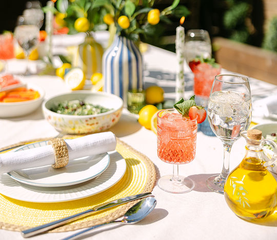 An outdoor table set for a summer backyard dinner party with colorful serveware and coastal Italian themed decor.