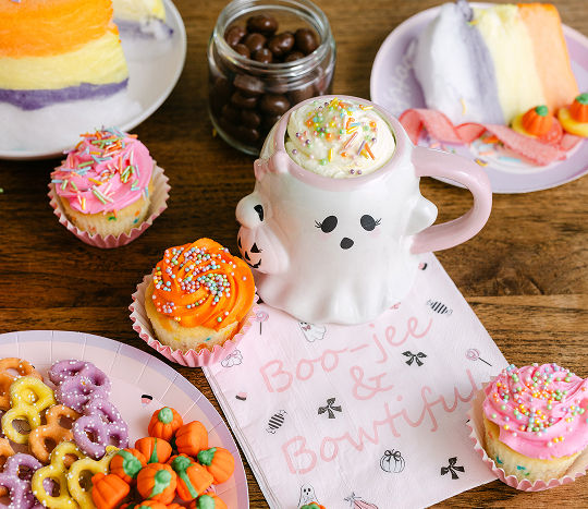 Close up of a summer Halloween themed party spread featuring summerween themed paper serveware with cupcakes, a cotton candy cake, and candy.