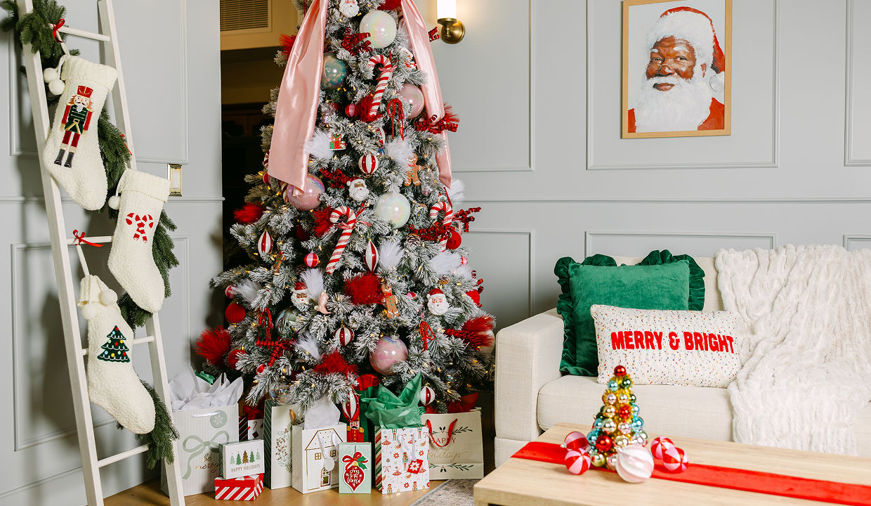A living room is decorated with a Christmas color palette including pink, red, green, and white with trendy Christmas decor accents like a framed Santa photo, jumbo bow tree topper, “merry & bright” throw pillow, stockings, and more elevated Christmas decorations from pOpshelf.