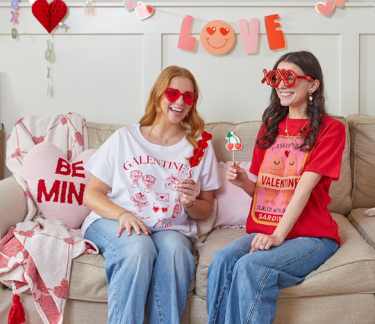 Friends in Valentine's t-shirts and heart-themed glasses holding Valentine's lollipops & cookies.