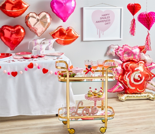 Galentine's Day party with rose foil balloon, lip and heart foil balloons, bar cart with pink wine glasses, heart-shaped chocolate fondue, pink cake stand, and more.