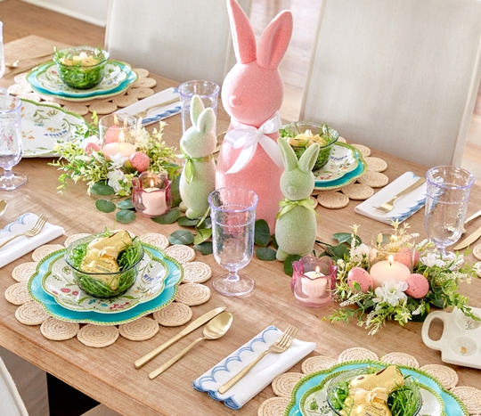 Dining table set for easter brunch with floral plates, platter & egg tray, glass goblets, and green glass bowls with a spring floral and flocked bunny centerpiece.