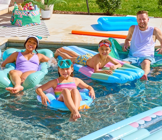 Mom, dad, and two kids in a swimming pool on color inflatable floats, swim rings, and rafts from pOpshelf.