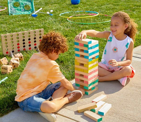 Kids in yard playing with wooden golf set, jumbo blocks and dice, giant 4-across game, pickle ball set, soccer set, and other outdoor toys from pOpshelf.