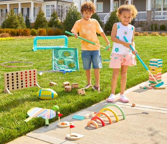 Kids in yard playing with wooden golf set, jumbo blocks and dice, giant 4-across game, pickle ball set, soccer set, and other outdoor toys from pOpshelf.