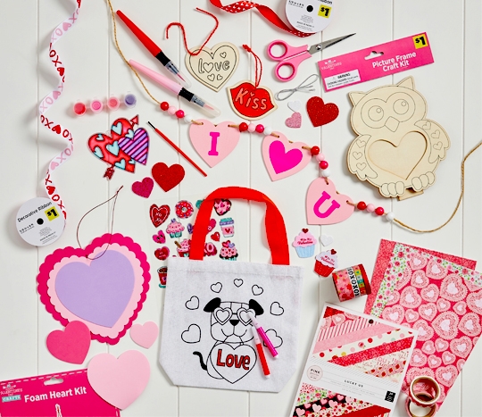 Valentine's Day crafts and supplies on a white table: foam hearts, DIY bags and wood crafts, stickers, ribbon & more.
