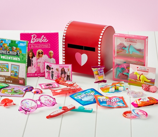 Red mailbox surrounded by Valentine's gifts, trinkets, and boxed Valentine's cards in various designs: Barbie, Minecraft, dinosaurs, and more.