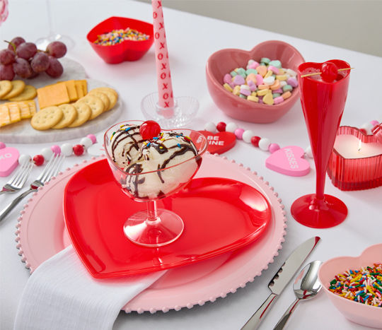 Romantic dinner table setting with pink charger, red heart plates, pink heart shaped ice cream dish, red heart champagne flute and more