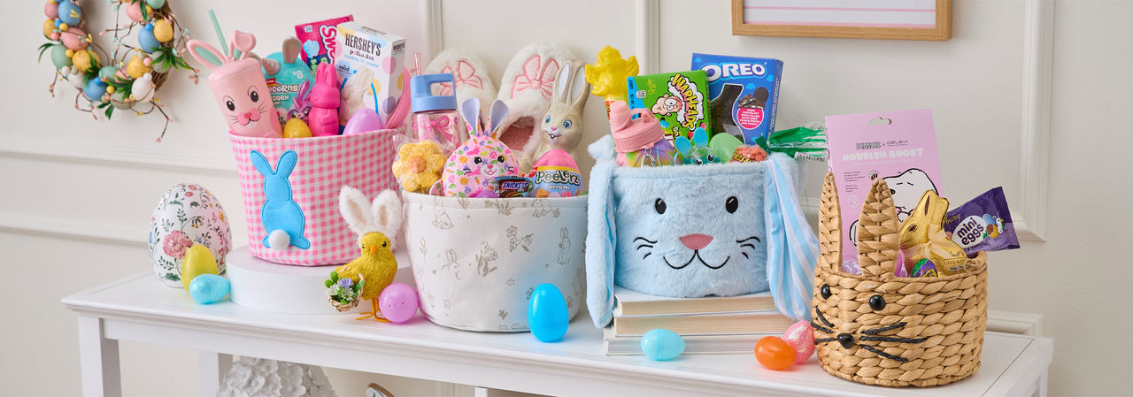 Four Easter baskets stuffed with plush, candy, eggs, grass & basket stuffers on a table decorated for Easter.
