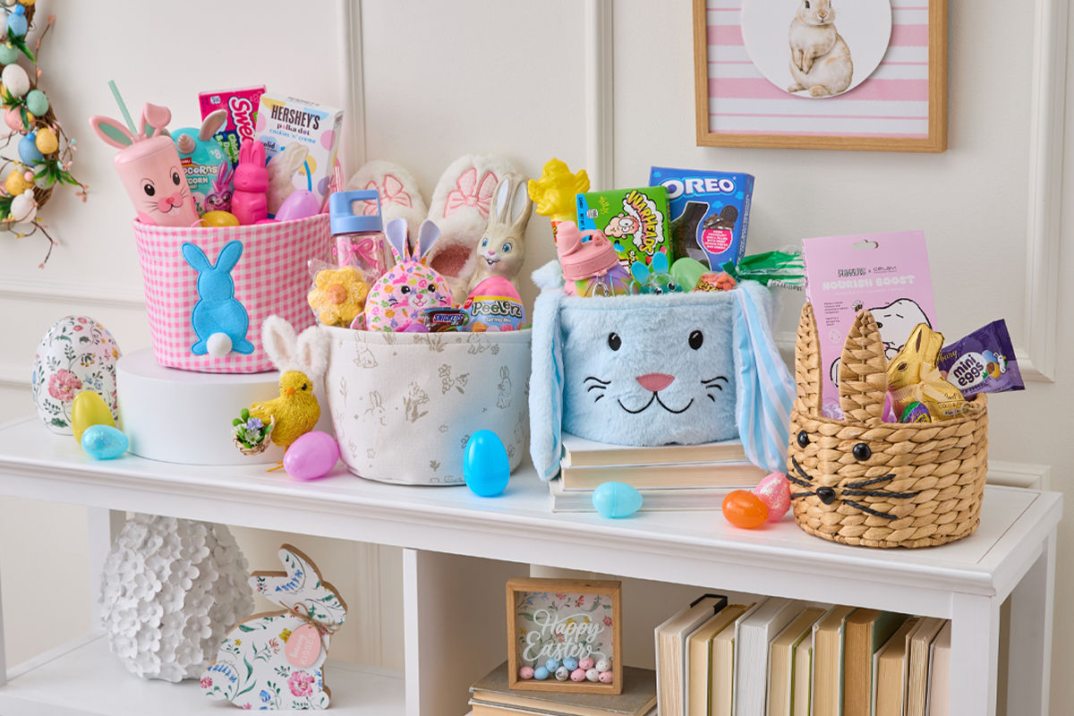 Four Easter baskets stuffed with plush, candy, eggs, grass & basket stuffers on a table decorated for Easter.