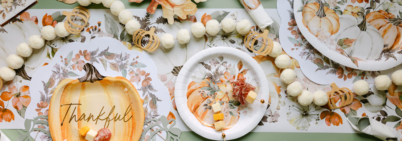 Fall party table set with pumpkin and leaf shaped plates, round harvest plates, napkins, gold party utensils, and fall & pumpkin table decor.